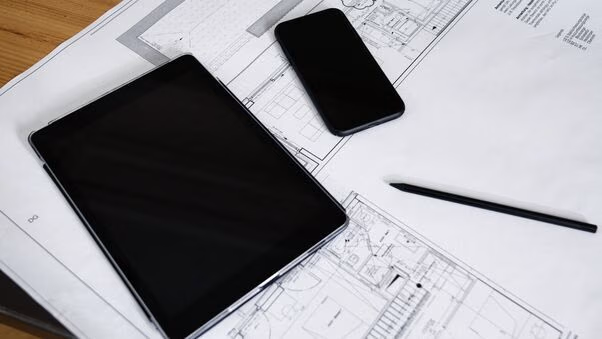 Ein Smartphone, ein Tablet und ein Bleistift liegen auf Bauplänen.