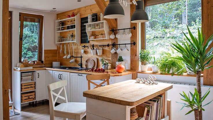 Das Foto zeigt eine große Küche mit vielen Aktzenten aus Holz. Die Küche ist halb weiß, halb braun gestrichen. Im Vordergrund steht ein Tisch, der ebenfalls aus Holz ist.
