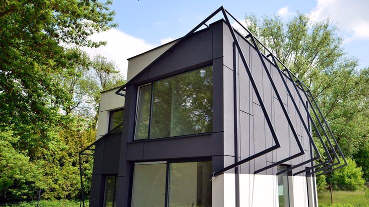 Abgebildet ist ein Haus im ganz speziellen Baustil mit schönem grünen Garten.
