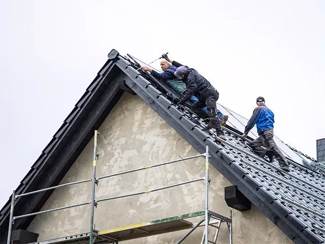 Mehrere Personen führen Arbeiten auf dem Dach eines Wohnhauses durch.