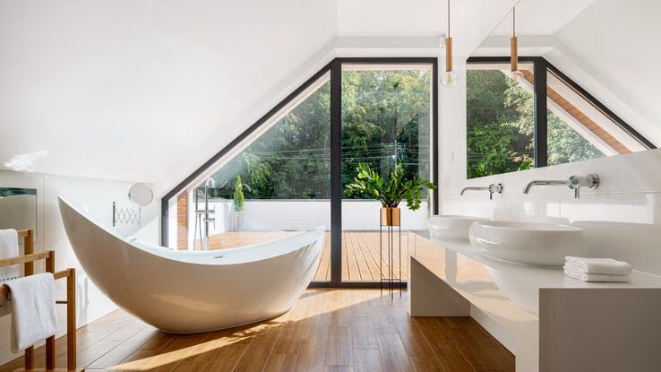 Ein Badezimmer mit großer freistehender Badewanne. Das bad hat bodentiefe Fenster und führt auf eine große Terrasse.