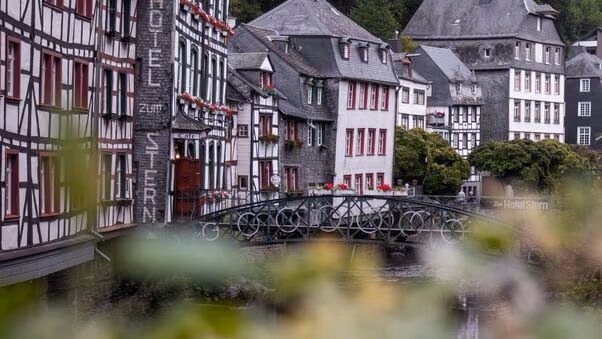 Das Foto zeigt viele ältere Häuser, die an einem Fluss liegen. Außerdem ist eine Brücke zu sehen. Die Häuser erinnern an Fachwerkhäuser. Sie haben typische Holzelemente, rote Fenster und graue Dächer.