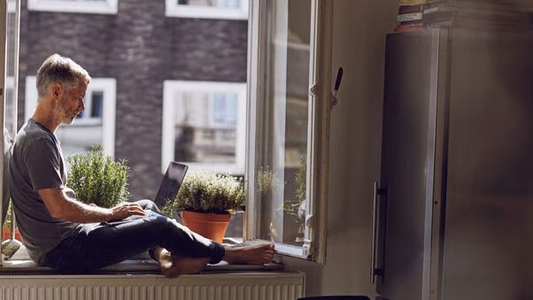 Ein Mann sitzt am Fenster und berechnet am Laptop die Instandhaltungskosten.