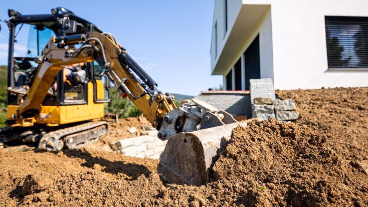Man sieht eine Baustelle mit einem Bagger im Vordergrund und dem Eigenheim im Hintergrund.