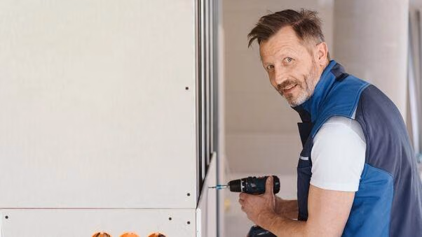 Das Foto zeigt einen Handwerker, der mit einem Akkuschrauber etwas zusammen baut. Er schaut lächelnd in die Kamera.