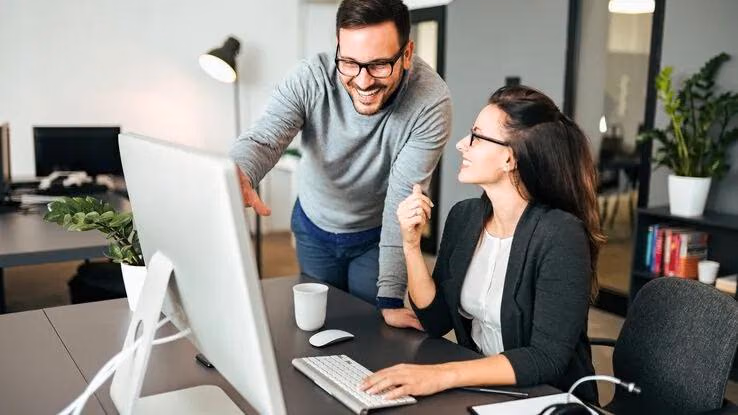 Ein Mann und eine Frau unterhalten sich an einem Computer in einem Büro.