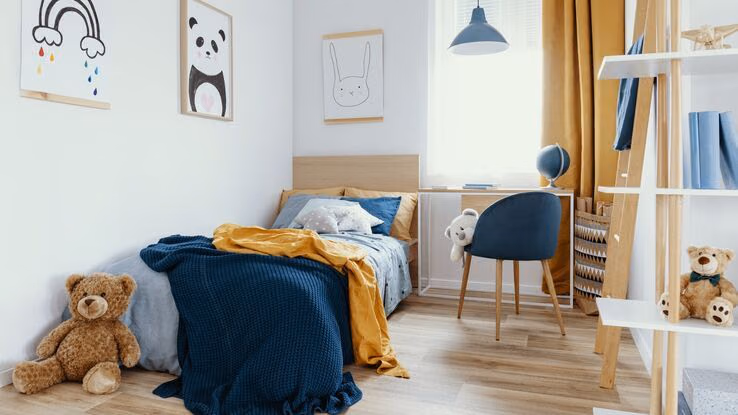 Ein Kinderzimmer in blau und orange gehalten. Es beinhaltet ein Bett, einen Schreibtisch und ein Regal.