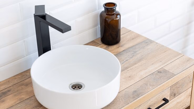 Man sieht ein Waschbecken auf einem Holztisch.