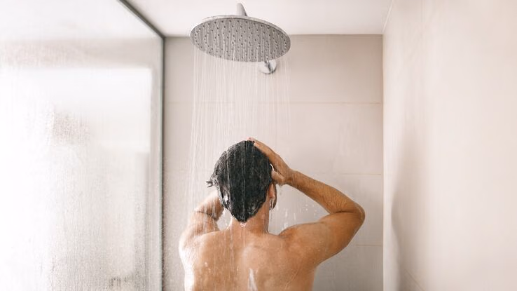 Ein Mann steht unter der Dusche und wäscht sich die Haare.