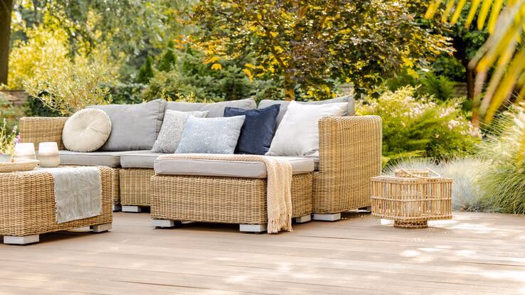 Ein gemütliches Outdoor-Sofa im Garten auf einer Holzterasse.