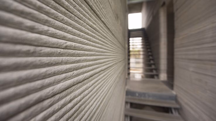 Das Foto zeigt eine Treppe und die Wand eines Gebäudes. Die Wand ist nicht aus Ziegel und Mörtel, sondern aus mehreren Beton Schichten.