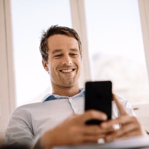 Person hält ein Smartphone vor hellem Fenster im Innenraum.