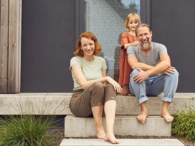 Eine Familie sitzt glücklich auf den Treppen vor Ihrem Haus.