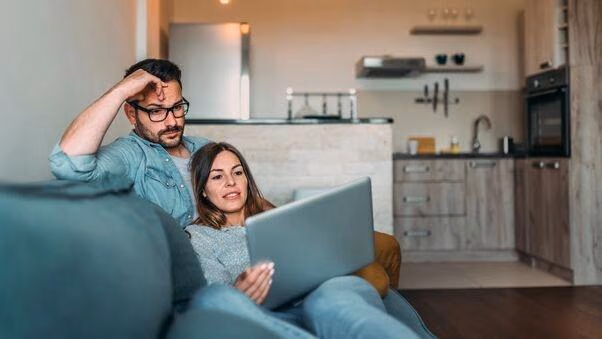 Ein Pärchen liegt auf dem Sofa und informiert sich über die Vor- und Nachteile eine Immobilie zu bauen oder zu kaufen.