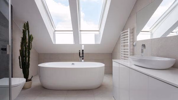 Es ist ein weiß eingerichtetes Badezimmer mit einer freistehendenden Badewanne und einem großen Dachfenster zu sehen.