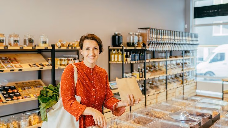Eine Frau hat im Supermarkt ihre Lebensmittel in einer Stofftasche und füllt etwas in einen Papierbeutel.