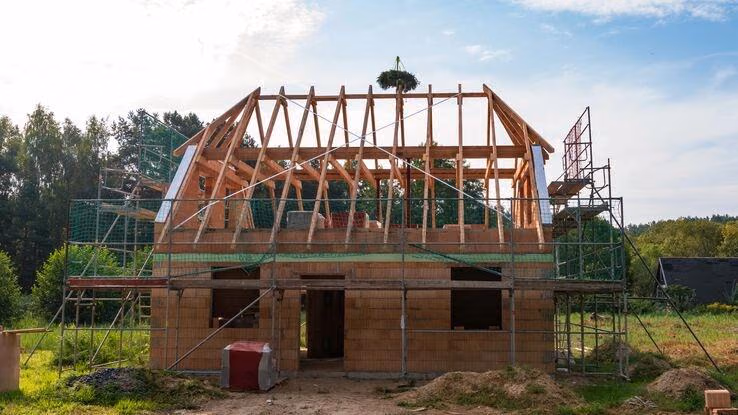 Abgebildet ist ein Haus im Bau. Der Dachstuhl steht, das Richtfest steht an.