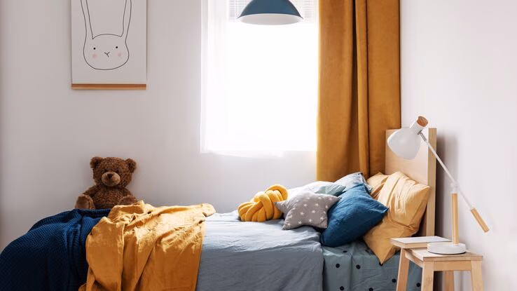 Ein Kinderbett und daneben ein Nachtkästchen mit einer Lampe darauf.