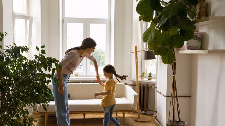 Eine Mutter und ihre Tochter tanzen gemeinsam in ihrem Wohnzimmer.
