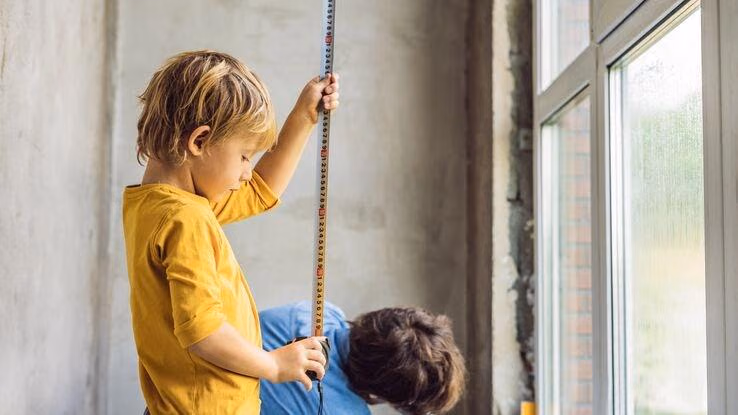 Ein Kind hilft seinem Vater beim Ausmessen der Fenster.