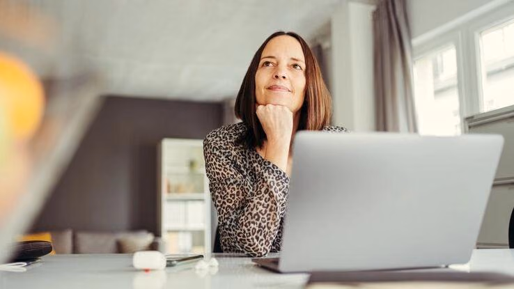 Eine Frau sitzt vor ihrem Laptop und überlegt.