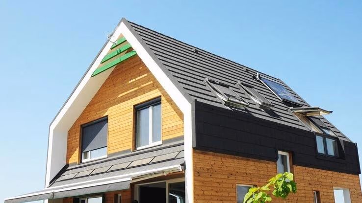 Auf dem Bild ist ein Haus mit einer Fassade aus hellem Holz und mit dunklem Dach abgebildet.
