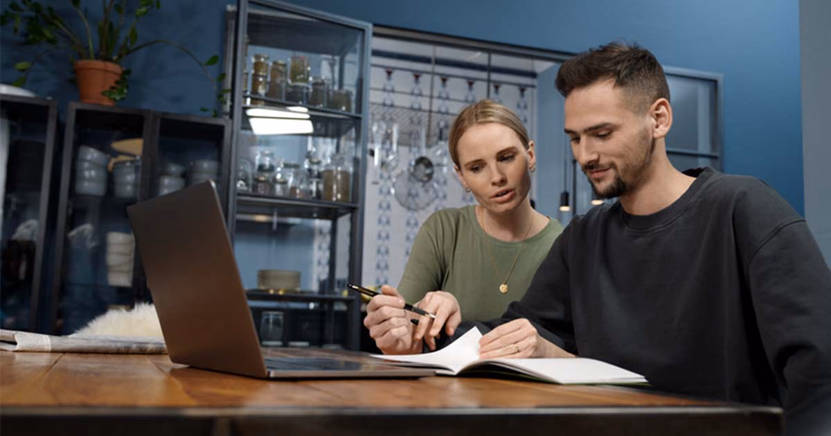 Ein junges Pärchen sitzt am Laptop und geht verschiedene Versicherungen für ihre Baufinanzierung durch.