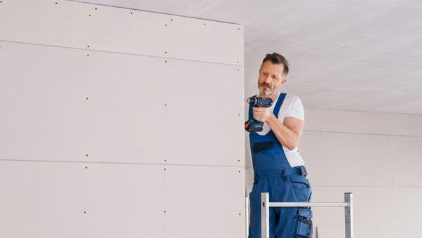 Ein Handwerker mit einer Bohrmaschine in der Hand bei der Installierung einer Trockenbauwand.