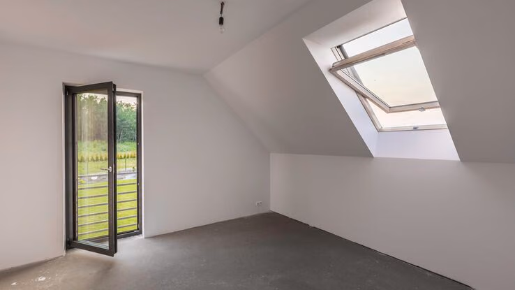 Man sieht einen leeren Raum mit einem Dachschrägenfenster und einem bodentiefen Fenster.