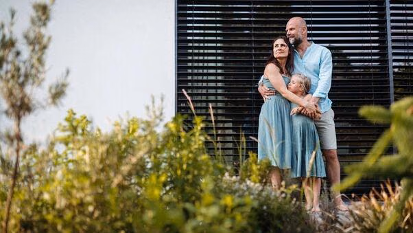 Eine Familie steht vor ihrer Immobilie im Garten.