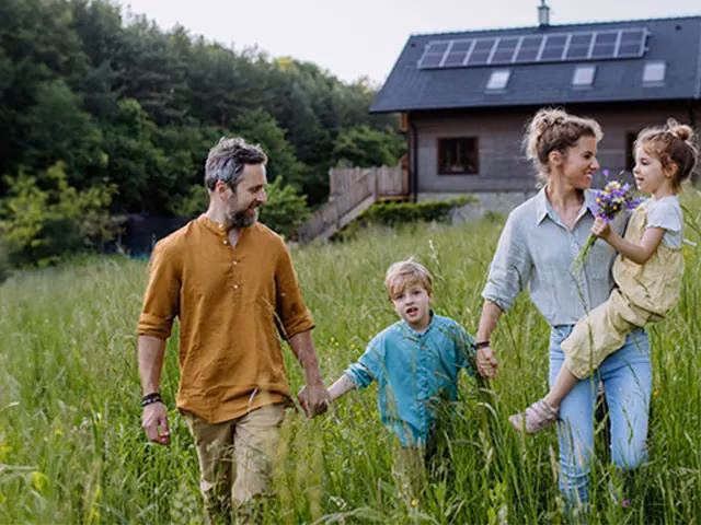 Eine Familie auf einem Feld. Im Hintergrund ist ein nachhaltig gebautes Haus zu sehen.