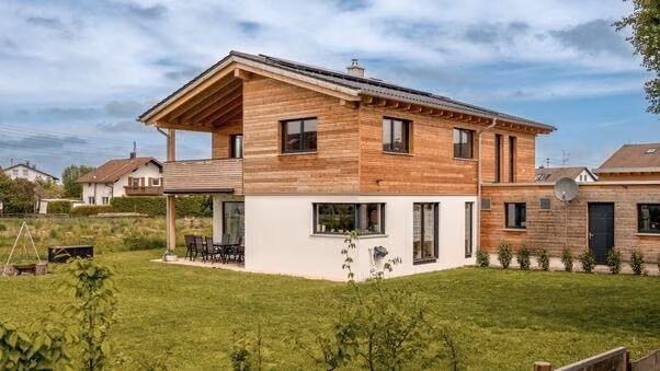 Ein modernes Einfamilienhaus mit großem Garten. Der erste Stock ist außen mit Holz verkleidet.
