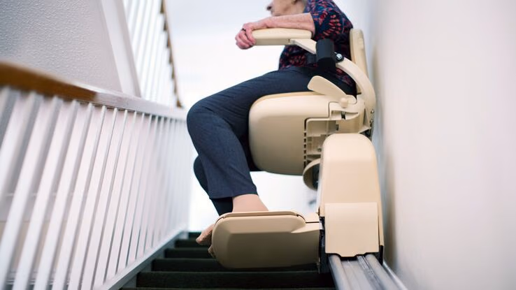 Ein Treppenlift hilft einer alten Frau in den ersten Stock zu kommen.