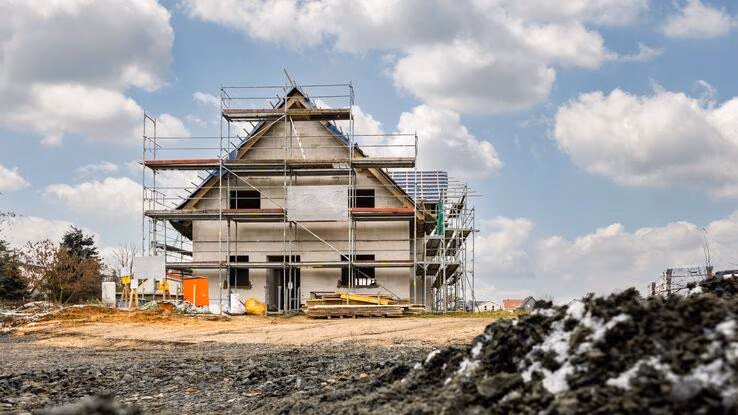 Auf einer Baustelle im Winter sieht man ein Neubau mit Gerüst.
