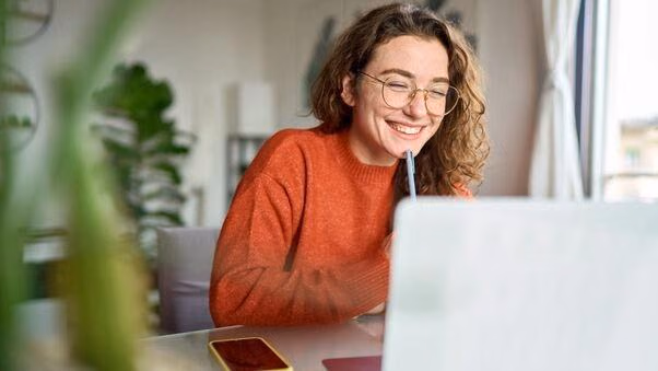 Eine Frau sitzt lachend vor dem Laptop an einem Schreibtisch.