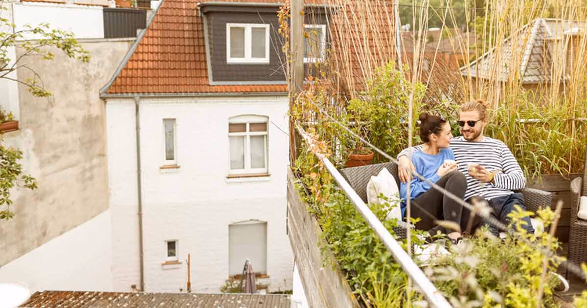 Ein Paar sitzt auf einem Balkon umgeben von Pflanzen und trinkt Kaffee.