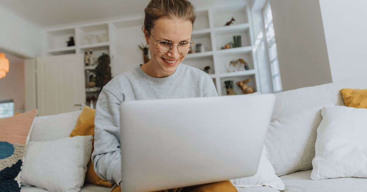 Eine Frau sitzt auf dem Sofa und arbeitet an ihrem Laptop.