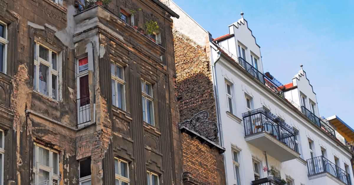 Zu sehen ist ein altes Mehrparteienhaus mit einer kaputten Fassade aus Holz.