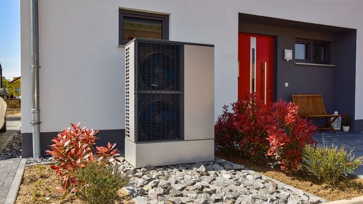Eine Wärmepumpe steht vor einem neugebauten Haus.