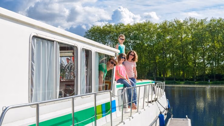 Das Foto zeigt eine Familie auf einem Hausboot. Es sind Mutter, Vater und zwei Töchter zu erkennen. Das Hausboot liegt aktuell an einem Steg.