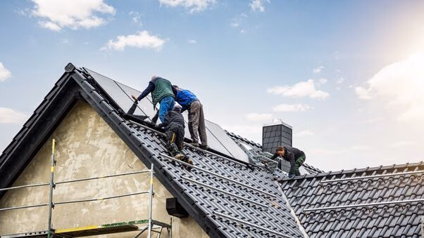 Vier Handwerker, die auf einem Dach Solarpanele anbringen.