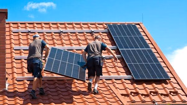 Zwei Handwerker montieren eine Photovoltaikanlage auf das Dach eines Hauses.