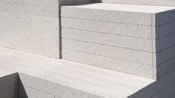 Das Foto zeigt viele Platten aus Beton. Sie sind aufeinander gestapelt und werden gelagert. Der Beton wurde als Quader geformt.