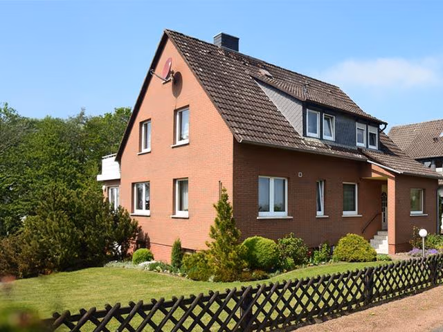 Zu sehen ist ein Einfamilienhaus mit Garten daneben und einem Zaun drum herum.