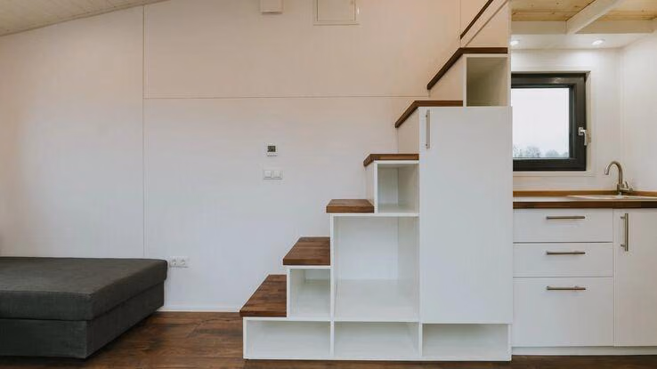 Das Foto zeigt ein Treppenregal. Es führt über die Küchenzeile in die obere Etage. Unter der Treppe befindet sich ein Regal und die Küchenzeile.
