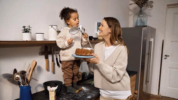Eine Mutter und ihre Tochter haben Kuchen gebacken. Das Kind schleckt den Löffel mit den Teigresten ab.