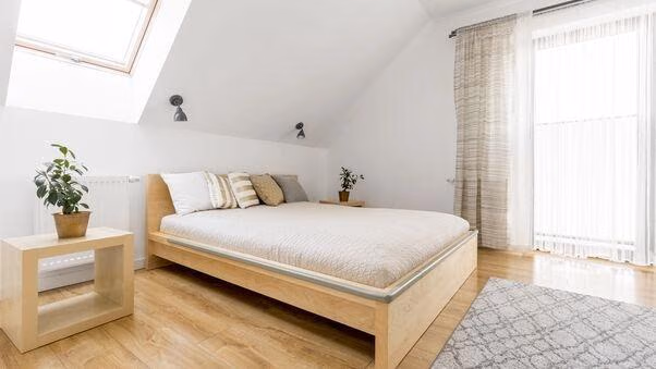 Ein großes Bett in Holzoptik. Durch eine große Balkontür fällt viel Licht.