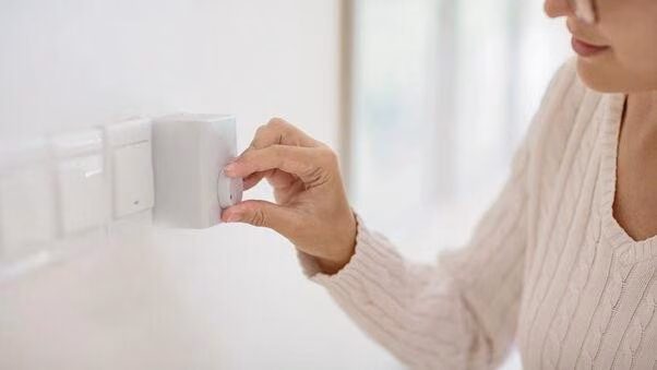 Eine Frau dreht die Heizung auf die richtige Raumtemperatur.