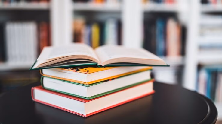 Drei Bücher liegen geschlossen übereinander. Ein viertes Buch liegt aufgeschlagen oben drauf.