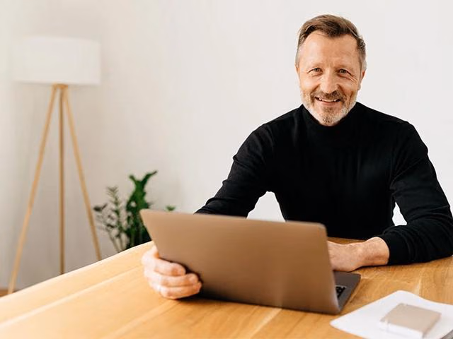 Ein Mann sitzt am Laptop und informiert sich über eine mögliche Baufinanzierung als Beamter.